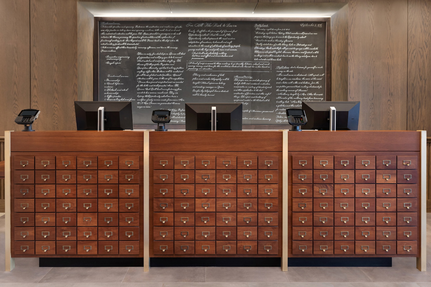 Check-in counters in the lobby use card catalogs of bygone days, flanked by a slate chalkboard— Photo by Hilton