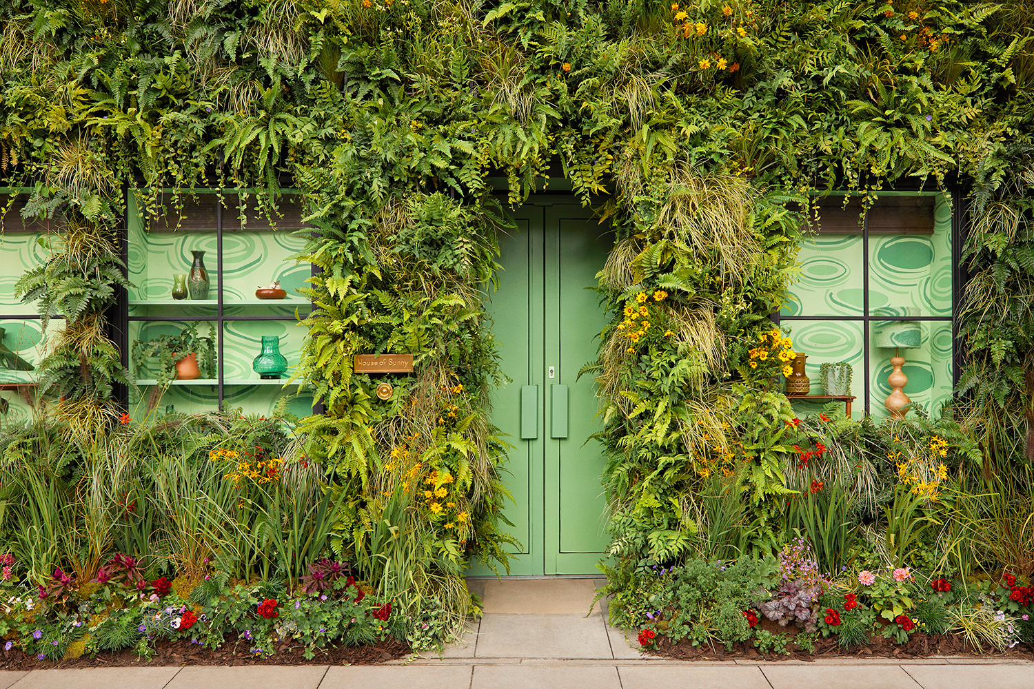 The green oasis entrance with real plants and flowers, inspired by the swirling green tones of Sunny’s famous Hockney Dress, as worn by celebrities. — Photo by Airbnb
